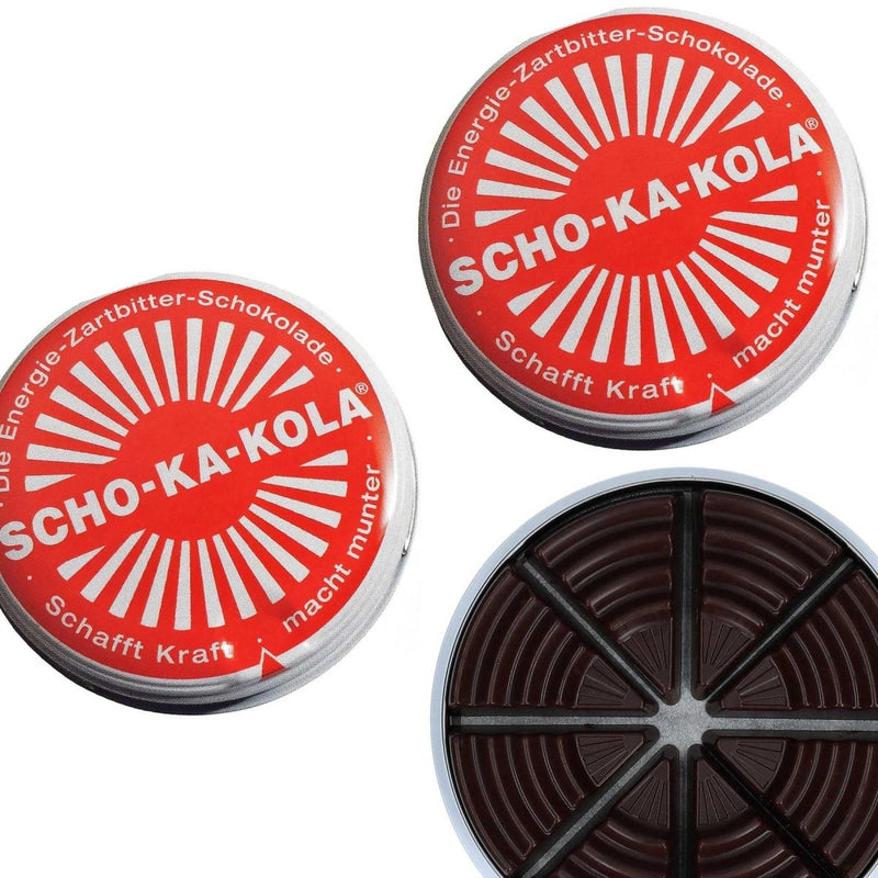 Two closed and one open 100g tin cans of German SCHO-KA-KOLA dark chocolate with caffeine segments visible inside.