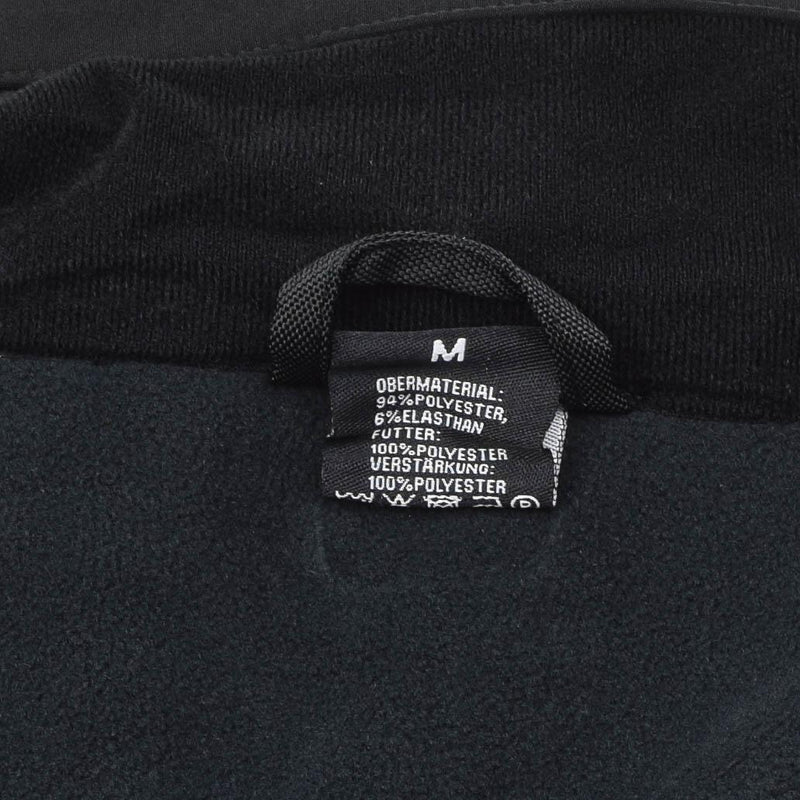 Close-up of MIL-TEC jacket fabric and size tag showing material composition and care details in black softshell material