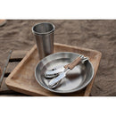 Lightweight stainless steel camping cutlery set with knife, fork, spoon, plate, and cup on wooden tray outdoors