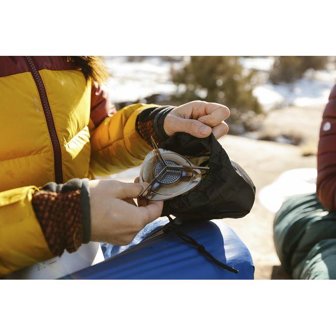 Person removing the compact Primus Essential Trail Stove from a black storage pouch outdoors in a snowy setting