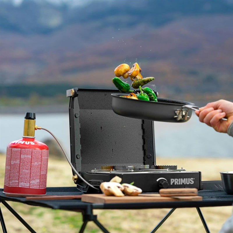 Primus Moja Stove compact outdoor gas burner cooking vegetables in pan by lake on portable camping table