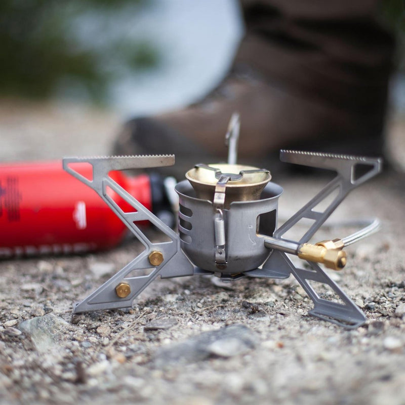 Compact Primus MultiFuel III hiking stove with high-output burner on rocky ground for outdoor camping use